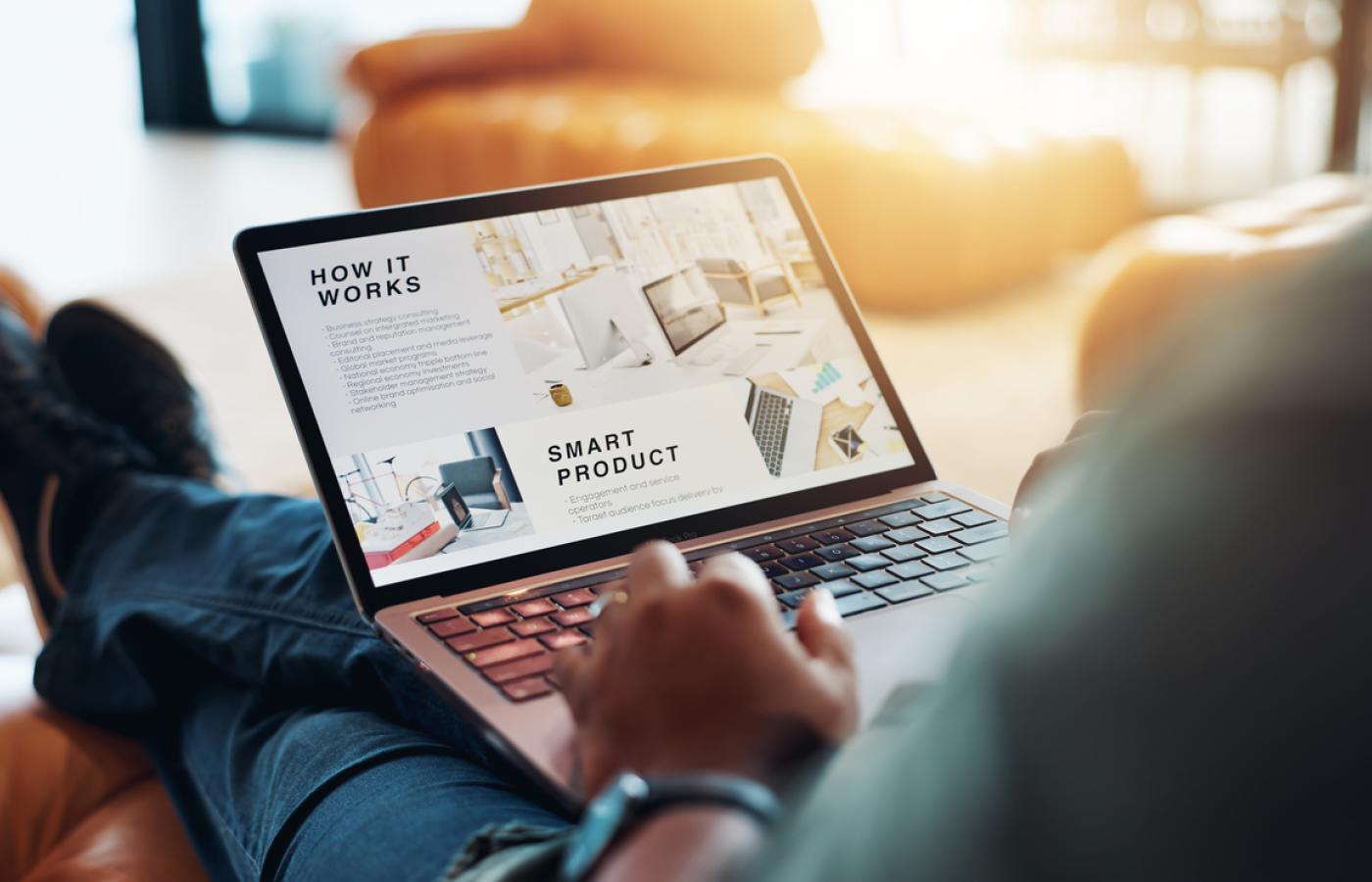 A laptop with a website on the screen sits on a mans legs.